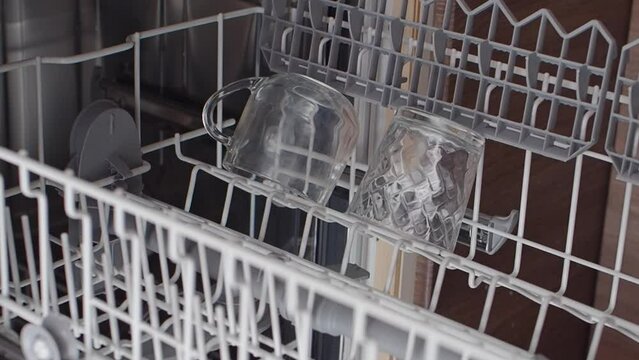 Close-up of female hands opening dishwasher with crystal clear glasses. Top view. Cleaning dirty dishes. Woman fills the upper level of the dishwasher with dirty dishes, glasses. Slow motion