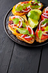 Healthy vegetarian toasts and lime on a black plate. Bruschetta with tomatoes, greens and olives. Healthy open sandwiches on black boards. Copy space. Top view