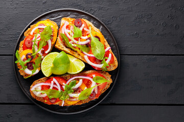 Healthy vegetarian toasts and lime on a black plate. Bruschetta with tomatoes, greens and olives. Healthy open sandwiches on black boards. Copy space. Top view