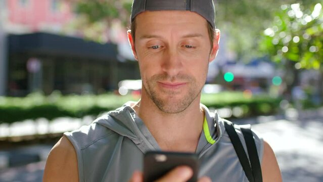 Young active man checking social media news updates on his phone after his exercise routine. An athletic and fit male browsing the internet giggles at clickbait on his cellphone outdoors in the city