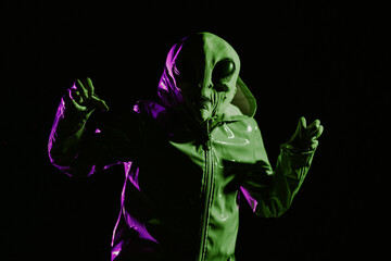 Futuristic alien showing frightening gesture, trying to scare. Creepy mask of humanoid on neon extraterrestrial planet masquerading as human person in smooth raincoat. UFO, fiction concept.