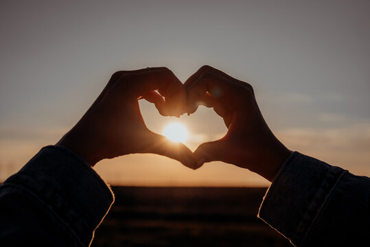 Woman making sign of shape heart. Silhouette of heart-shaped hands on sun flares background. Volunteering, donation help and love concept.
