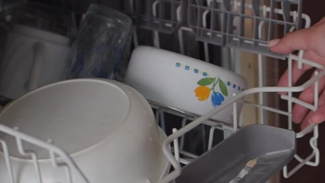 Housewife puts dirty dishes in the dishwasher. Female hands unload the dishwasher in close-up. Modern household appliances at home. Woman puts the top baskets with dirty dishes in the dishwasher. Slow