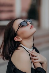 a brunette girl in a black jacket and dress and black glasses sits in a cafe