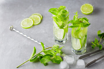 Mojito cocktail on a gray background. Two glasses of cocktail with mint, lime and ice. Bar tools and ingredients for cocktail