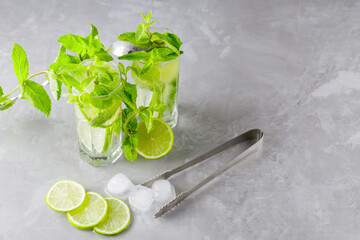 Mojito cocktail on a gray background. Two glasses of cocktail with mint, lime and ice. Bar tools and ingredients for cocktail