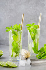 Mojito cocktail on a gray background. Two glasses of cocktail with mint, lime and ice. Bar tools and ingredients for cocktail