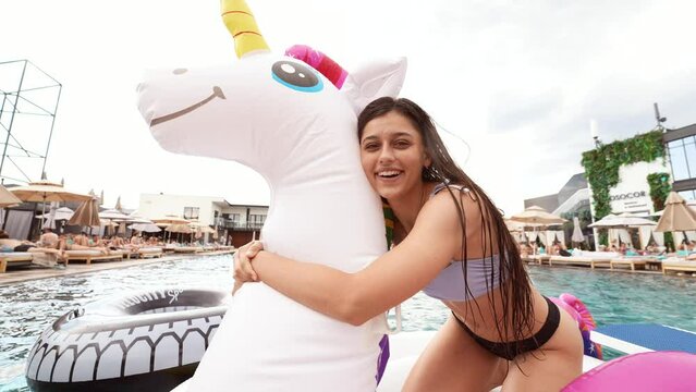 Woman in bikini in inflatable unicorn toy mattress float in pool.