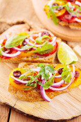 Spanish tapas and lime on a cutting board. Bruschetta with tomatoes, greens and olives. Healthy open sandwiches on wooden boards. Top view