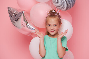 Joyful child girl in elegant tulle dress near the balloons. Birthday present. Funny face celebrates...