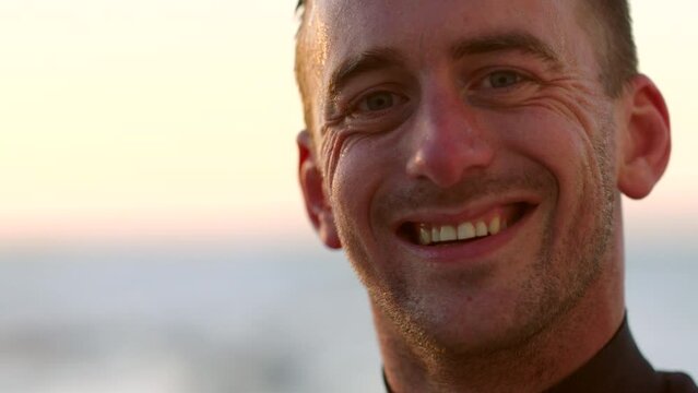 Face of a happy surfer tired and resting after a water sport workout on holiday. Closeup portrait of a tired man looking exhausted after exercise at the beach at sunset against a blurred background
