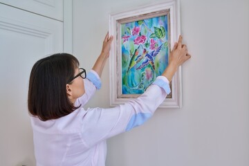 Woman hanging floral birds art framed at home on the wall