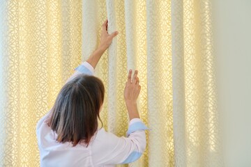 Woman touches curtains, lays out the folds on light velvet curtain