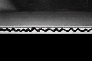 A wavy line of black silicone sanitary sealant on the rim of an artificial stone sink. Abstract black and white background, place for text