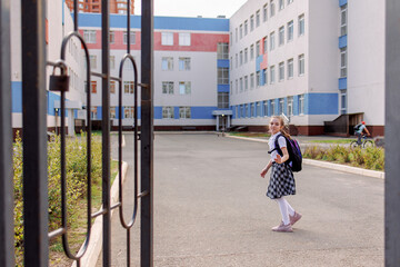 Back to school. Girl in school uniform go to school with backpack behind their backs. Kid waving her hand saying bye. Beginning of lessons. First day of autumn. Elementary school student. 