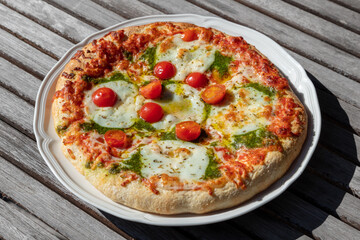 Vegetarian pizza with mozzarella cheese on a plate outdoors on wooden table