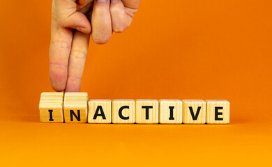 Active or inactive symbol. Businessman turns wooden cubes and changes the word Inactive to Active. Beautiful orange table orange background, copy space. Business and active or inactive concept.