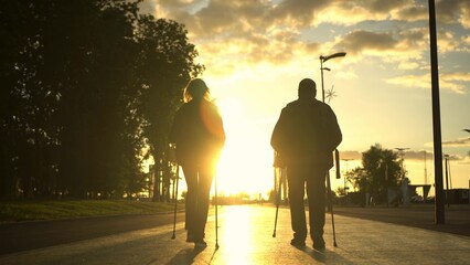 An elderly couple is engaged in Nordic walking in the park going into the sunset. A man and a woman...