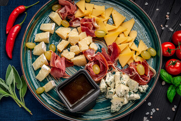 Cheese platter with different cheese, jamon, prosciutto and grapes.