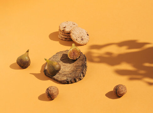 Vintage style composition made of figs on wooden podium, cookies and nuts on orange background. Retro style food concept.