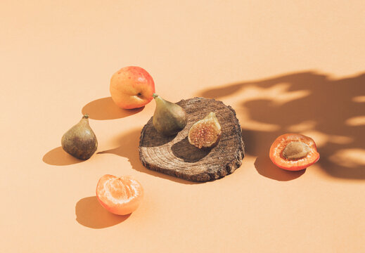 Vintage style composition made of figs on wooden podium, apricots and tree shadow on orange background. Retro style food concept.