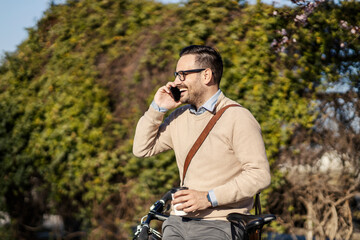 A man in public park leaning on bicycle, talking on the phone and taking a break.