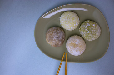 Chopsticks and traditional Japanese dessert mochi or daifuku in rice dough close-up. Four mochi ice cream balls on gray plate on blue-violet table selective focus. Asian sweet delicious food dessert.