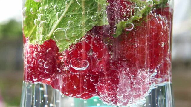 Close up view at raspberries and mint leaves in soda with bubbles.