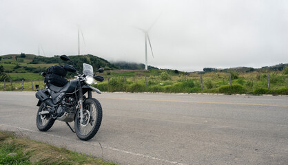 Dual purpose motorbike on roads mountain of Peru. Grey sky and wind turbinesand are background