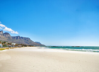 Copy space at sea with a clear blue sky and mountain in the background. Calm ocean waters washing onto an empty beach shore. Peaceful scenic coastal landscape for a relaxing and zen summer getaway