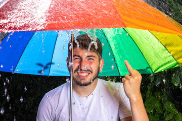 image amusante d'un jeune homme sous un parapluie par temps d'orage qui grimace et qui fait un...