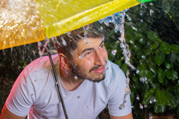 image amusante d'un jeune homme sous un parapluie. Il est sous un orage et il pleut beaucoup. Il...