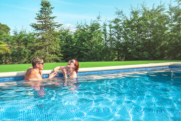 two friends laughing out loud, cooling off together in the pool on a sunny summer day. mother and...