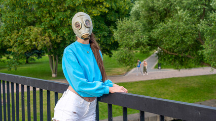 A girl in a gas mask stands on a bridge across the river. Alienation in the city. Fashion, ecology...