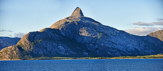 Scenic view a mountain lining a coast in Bodo, Norway. An expansive natural vista of a spring lake during sunrise in the morning. Remote, lush vegetation alongside a lake in a European destination