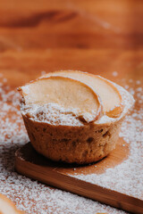 Cupcake casero con rodajas de manzana, rodeado de azúcar encima de mesa de madera, deliciosos dulces de pastelería, desayuno rústico de manzana