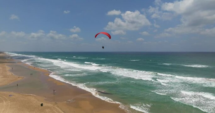 Powered Paraglide flying above a sunny beach.
