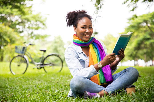 Charming gay woman reading book in grass under tree with cup of coffee and bicycle. Relax in summer time holiday laying on the grass field. Independence and polygamy. Supporters of the LGBT community