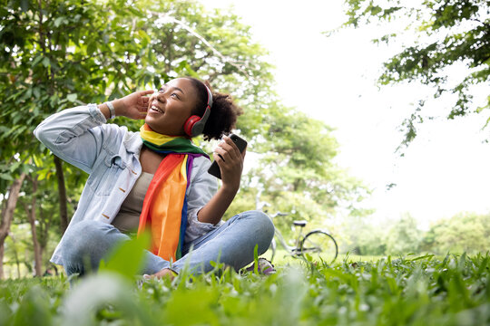 Charming gay woman listening music under tree with smartphone and bicycle. Relax in summer time holiday laying on the grass field. Independence and polygamy. Supporters of the LGBT community