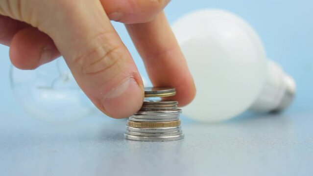 A stack of coins, money on the background of an energy-saving LED lamp and a classic glass incandescent lamp. Money, electricity bill. Payment of expenses for electric light, lighting.