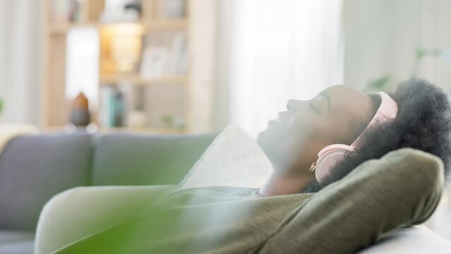 Young woman listening to music while relaxing on a sofa at home. Carefree, cheerful and happy female wearing headphones while enjoying a podcast and favourite songs. Taking a break to rest in comfort