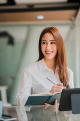 Freelance Asian woman working on a computer tablet in a modern office. make an account analysis report on real estate investment information financial system concept and tax vertical picture