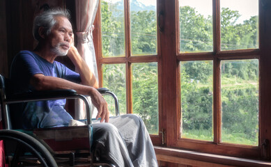 The old man sat in a wheelchair alone, looking at the window.