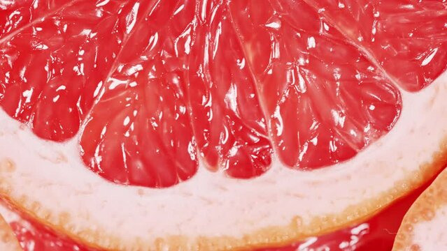 Slow motion of rotation ripe sliced grapefruites. Circles of fresh citrus as food background. Tropical fruits. Concept of proper nutrition or healthy lifestyle. Macro shot.