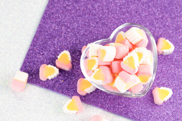 Obraz na płótnie Canvas Colorful miniature marshmallows in a love shape glass on a purple white background