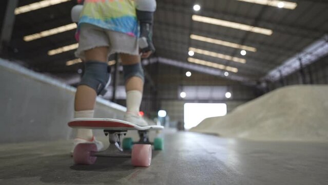 closeup skate wheel and foot or leg on back of asian child or kid girl playing skateboard or surfskate and start carving in indoor track skatepark by extreme sports to wearing body safety knee support