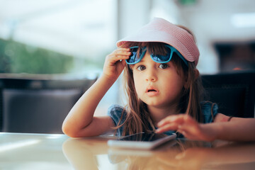 Funny Girl Taking Off Sunglasses to Check Mobile Phone. Child spending screen time in a restaurant...