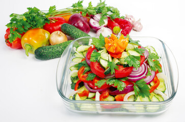 Salad of fresh vegetables in a glass salad bowl and individual vegetables on white.