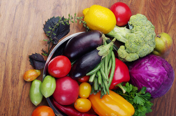 Fresh vegetables eggplant, tomatoes, cucumbers, peppers, green beans on a wooden table.