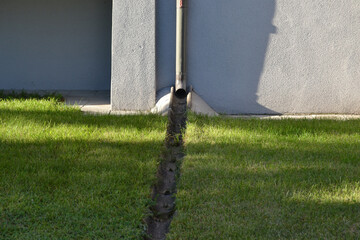 A metal pipe for draining water against the background of a building wall. Concrete trench on a green grassy carpet for water drainage.